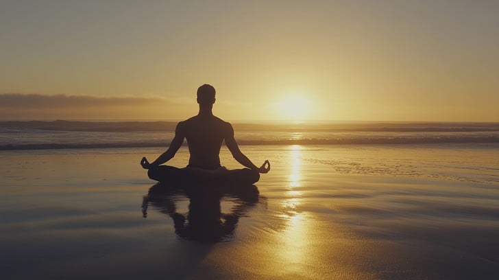 A person sitting peacefully on a beach at sunrise